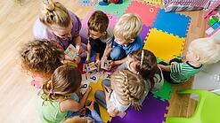 Kindergartenkinder sitzen in einem Kreis und lernen Buchstaben mit einer Erzieherin.