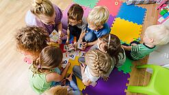 Kindergartenkinder sitzen in einem Kreis und lernen Buchstaben mit einer Erzieherin.