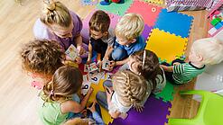 Kindergartenkinder sitzen in einem Kreis und lernen Buchstaben mit einer Erzieherin.