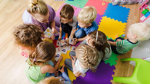 Kindergartenkinder sitzen in einem Kreis und lernen Buchstaben mit einer Erzieherin.