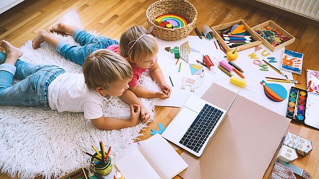 Zwei Kinder liegen auf dem Boden und schauen in einen Laptop.
