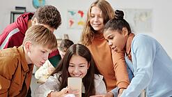 Mädchen mit Smartphone in der Hand wird von einer Gruppe anderer Jugendlicher umringt.