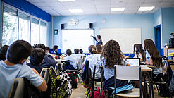 Schülerinnen und Schüler sitzen in einem Klassenraum und schauen auf die Tafel.