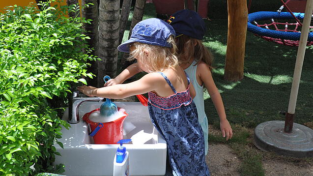 Zwei Kindergartenkinder befüllen einen Wassereimer.