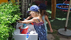 Zwei Kindergartenkinder befüllen einen Wassereimer.