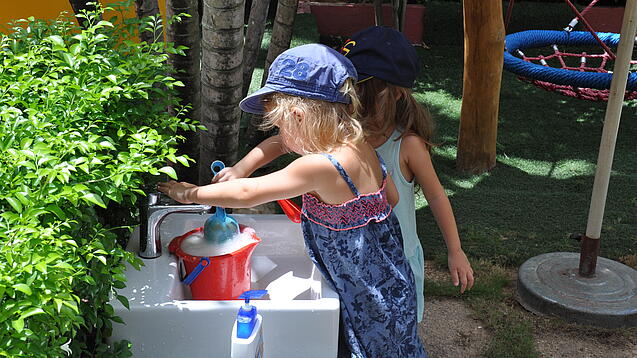 Zwei Kindergartenkinder befüllen einen Wassereimer.