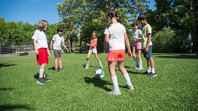 Mehrere Kinder spielen Fußball. Sie stehen dabei in einem Kreis.