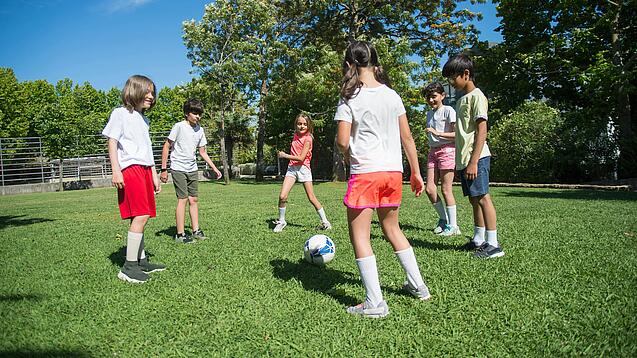 Mehrere Kinder spielen Fußball. Sie stehen dabei in einem Kreis.