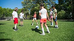 Mehrere Kinder spielen Fußball. Sie stehen dabei in einem Kreis.
