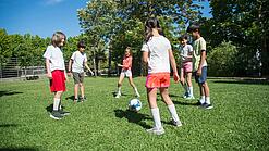 Mehrere Kinder spielen Fußball. Sie stehen dabei in einem Kreis.