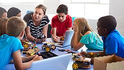 Eine Gruppe Kinder im Grundschulalter sitzt in einem Kreis und bekommt etwas erklärt.