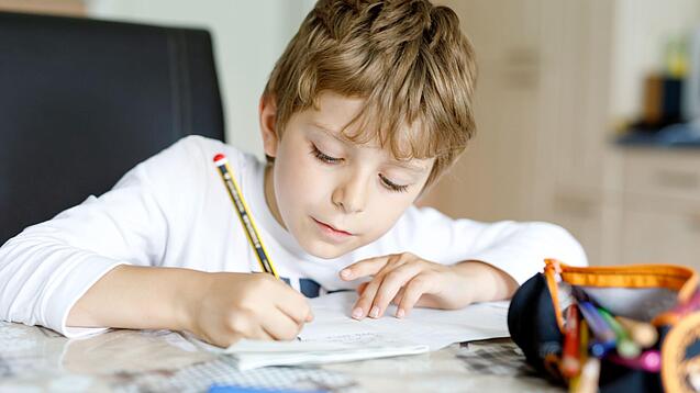Ein junger Schüler schreibt auf ein Blatt Papier.