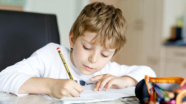 Ein junger Schüler schreibt auf ein Blatt Papier.