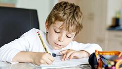 Ein junger Schüler schreibt auf ein Blatt Papier.