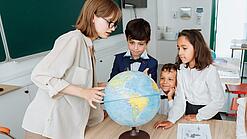 Junge Lehrerin und Schulkinder schauen sich einen Globus an.