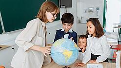 Junge Lehrerin und Schulkinder schauen sich einen Globus an.