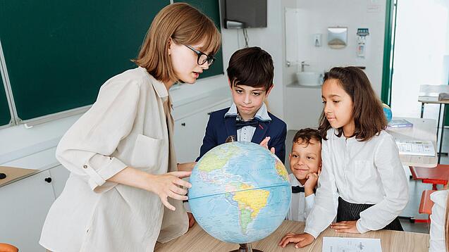 Junge Lehrerin und Schulkinder schauen sich einen Globus an.