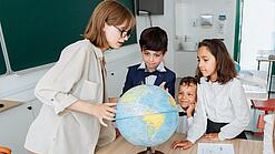 Junge Lehrerin und Schulkinder schauen sich einen Globus an.