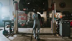 Ein Automechaniker betrachtet die Unterseite eines Autos auf einer Hebebühne.