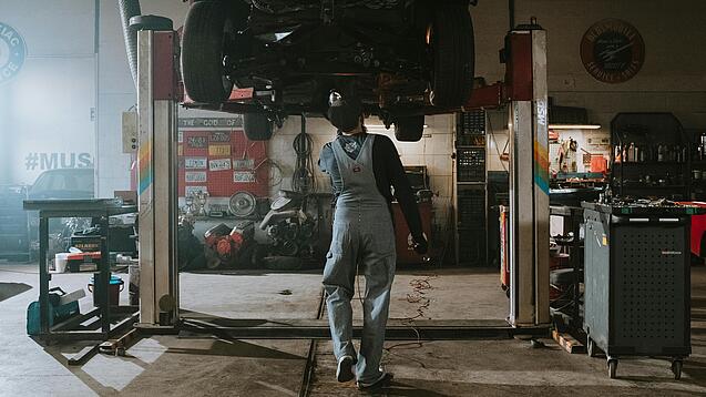 Ein Automechaniker betrachtet die Unterseite eines Autos auf einer Hebebühne.