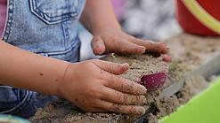 Kinderhände schaufeln Sand in ein Sandförmchen.