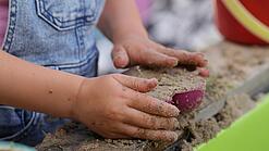 Kinderhände schaufeln Sand in ein Sandförmchen.