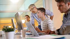 Ein Lehrer hilft Schülern, die an einem Computer arbeiten.