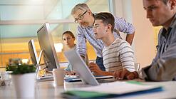 Ein Lehrer hilft Schülern, die an einem Computer arbeiten.