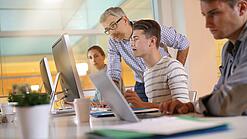 Ein Lehrer hilft Schülern, die an einem Computer arbeiten.