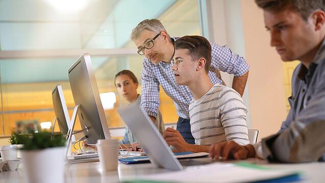 Ein Lehrer hilft Schülern, die an einem Computer arbeiten.