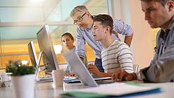 Ein Lehrer hilft Schülern, die an einem Computer arbeiten.