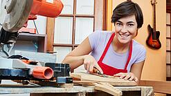 Eine junge Frau arbeitet mit einem Werkzeug an einem Holzinstrument.