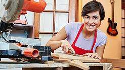Eine junge Frau arbeitet mit einem Werkzeug an einem Holzinstrument.