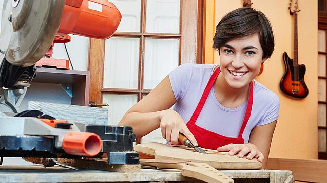 Eine junge Frau arbeitet mit einem Werkzeug an einem Holzinstrument.