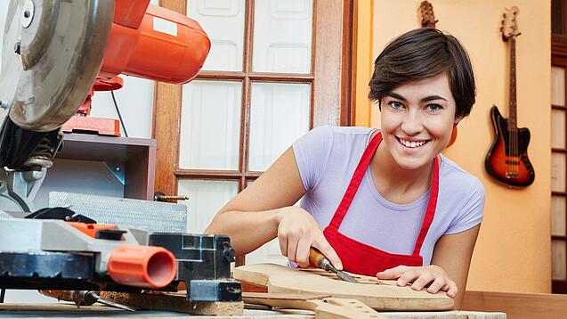 Eine junge Frau arbeitet mit einem Werkzeug an einem Holzinstrument.