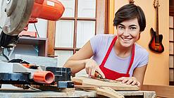 Eine junge Frau arbeitet mit einem Werkzeug an einem Holzinstrument.