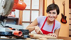 Eine junge Frau arbeitet mit einem Werkzeug an einem Holzinstrument.