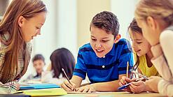 Schulkinder sitzen an einem Gruppentisch und schreiben etwas auf.