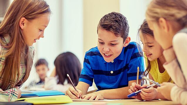 Schulkinder sitzen an einem Gruppentisch und schreiben etwas auf.