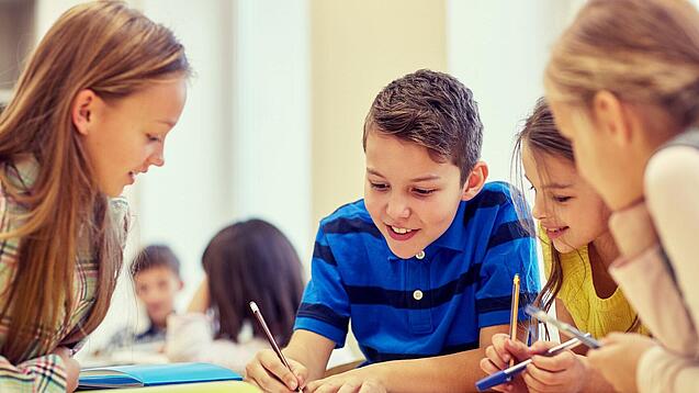 Schulkinder sitzen an einem Gruppentisch und schreiben etwas auf.