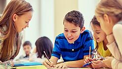 Schulkinder sitzen an einem Gruppentisch und schreiben etwas auf.