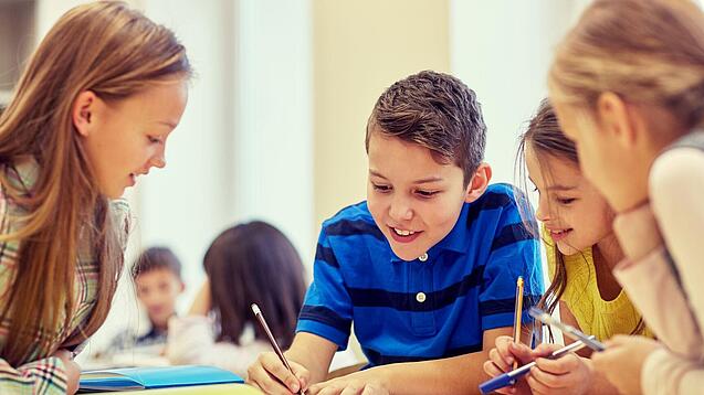 Schulkinder sitzen an einem Gruppentisch und schreiben etwas auf.