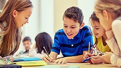 Schulkinder sitzen an einem Gruppentisch und schreiben etwas auf.