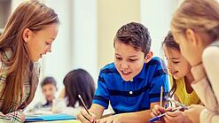 Schulkinder sitzen an einem Gruppentisch und schreiben etwas auf.