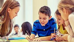 Schulkinder sitzen an einem Gruppentisch und schreiben etwas auf.