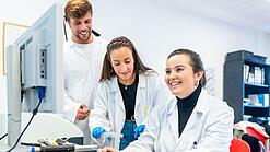 Drei Wissenschaftlerinnen sitzen vor einem Computer und lächeln.