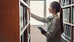 Eine junge Frau greift nach Büchern in einem Regal.