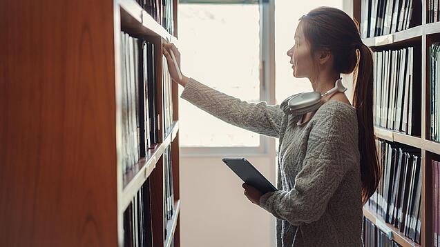 Eine junge Frau greift nach Büchern in einem Regal.