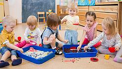 Eine Gruppe Kleinkinder spielt mit Behältern mit Sand und Kaffeebohnen.