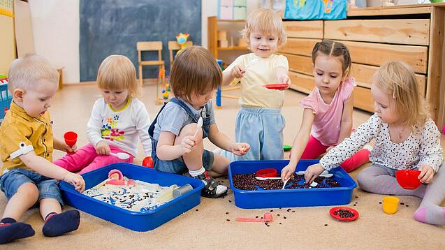Eine Gruppe Kleinkinder spielt mit Behältern mit Sand und Kaffeebohnen.
